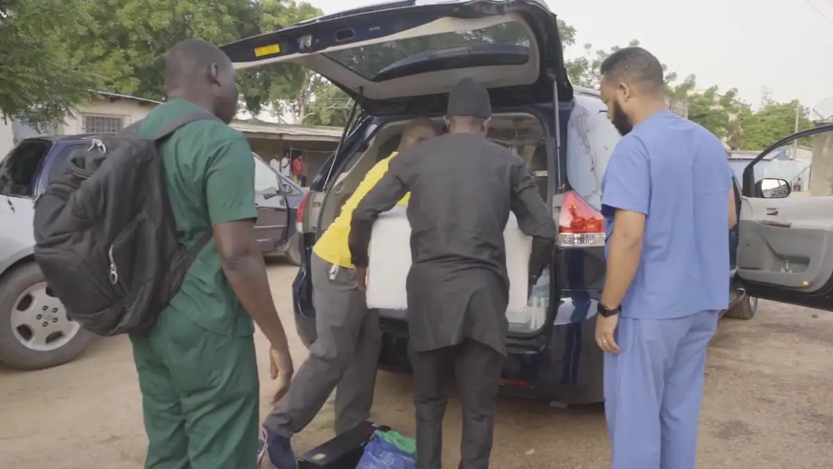 Three members of the outreach team in green tops with a child under a shelter in Kano State.
